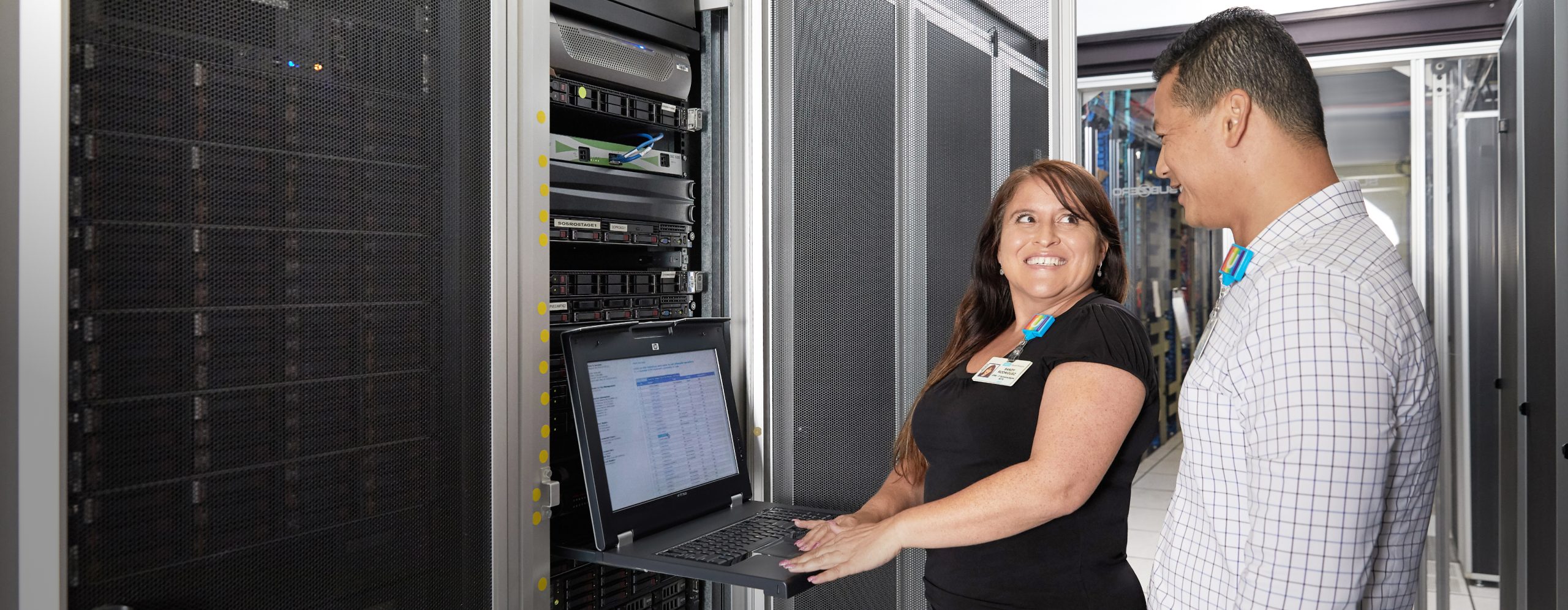 Smiling male and female UCLA Health information technology professionals working together in a large computer server room