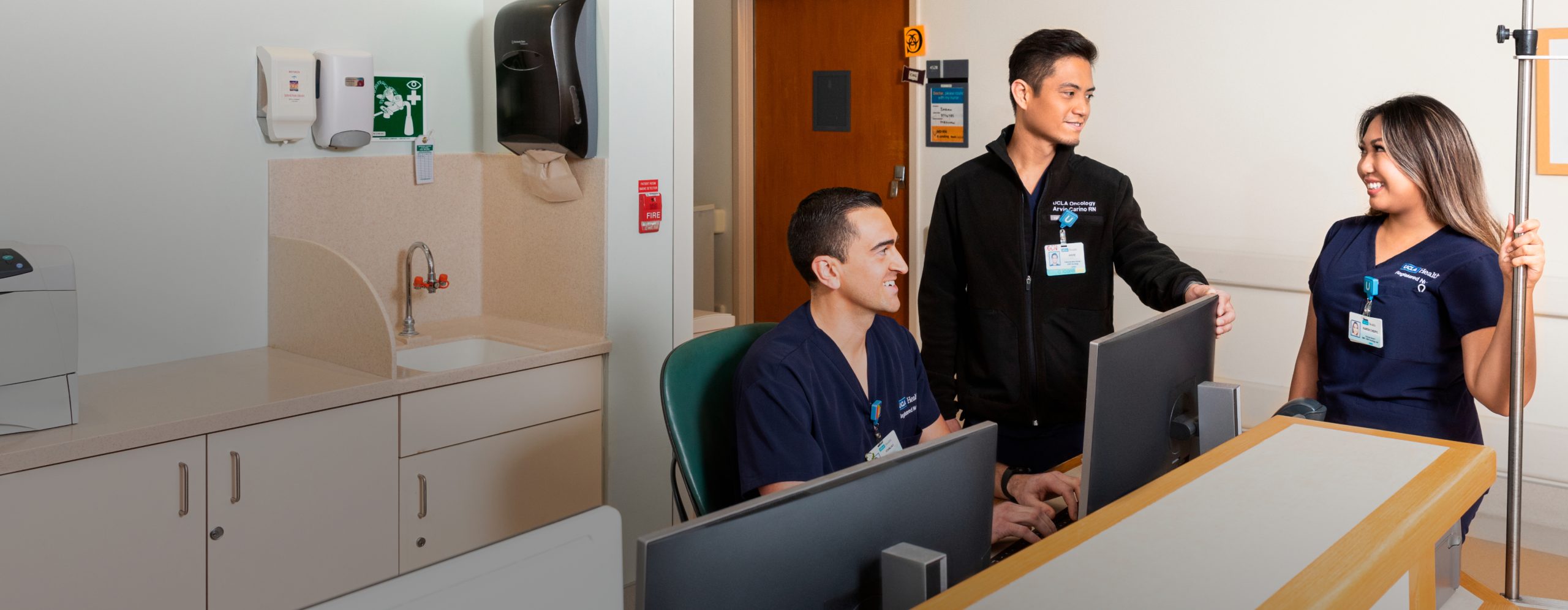 Two male and one female UCLA Health new grad nurses conversing at a UCLA Health hospital nurses’ station